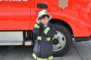 消防士の服を着て、消防車と記念撮影をする子ども