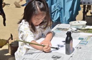 竹で作った筆で文字を書く子ども